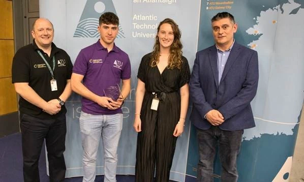 Photograph of four people standing indoors in front of a backdrop featuring Atlantic Technological University branding and a map. One person holds a glass award.