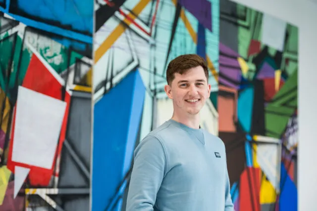 Male student in blue jumper standing in front of large artwork