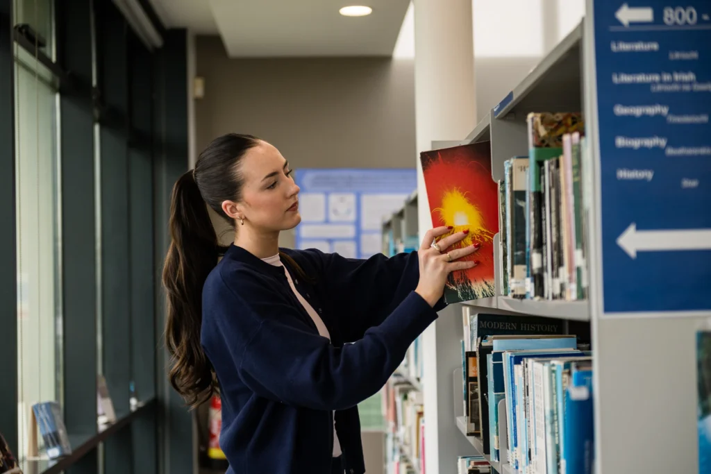 Female student taking book from shelf in library at ATU St Angelas campus