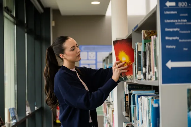 Female student taking book from shelf in library at ATU St Angelas campus