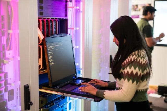 Student coding on a laptop beside a server unit that has colourful LED lighting