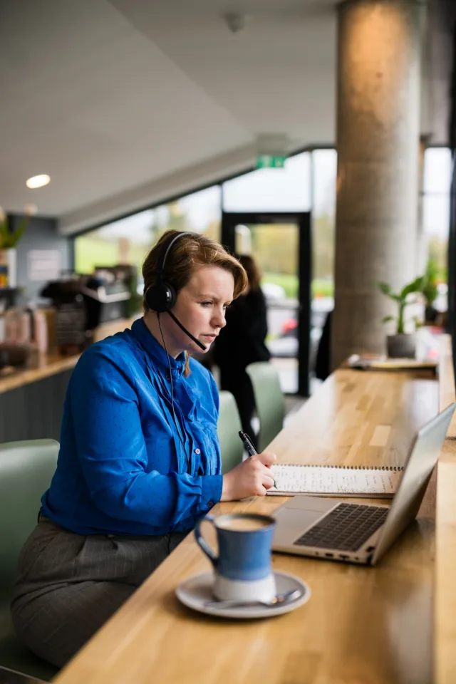 Mature student in blue shirt watching an online lecture on her laptop in a café