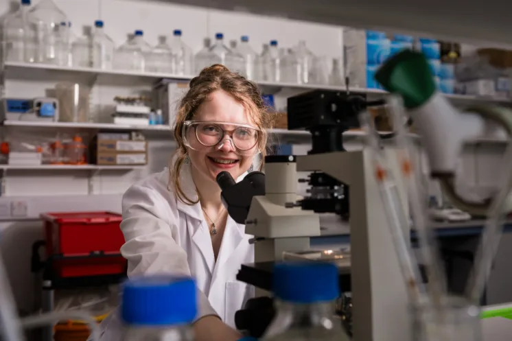 Researcher in a lab smiling at microscope