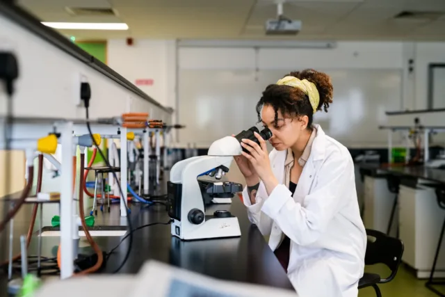 Researcher in lab coat looking into microscope