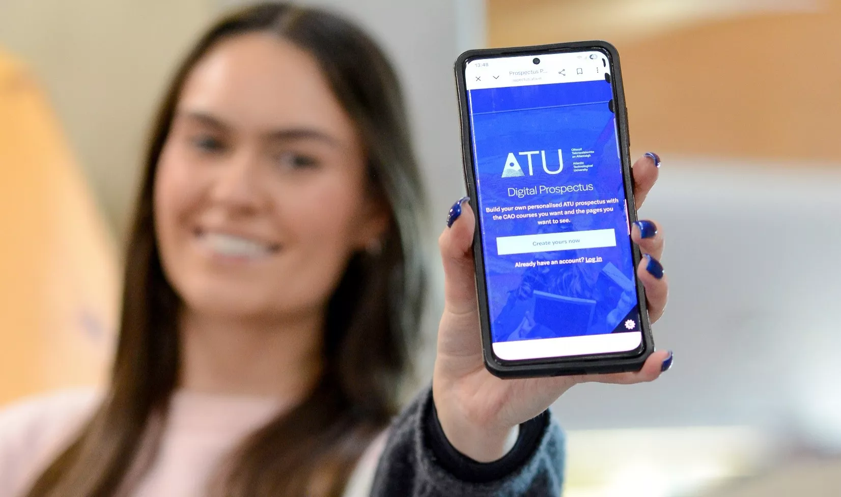 Person holding a smartphone towards the camera displaying the ATU Digital Prospectus webpage.