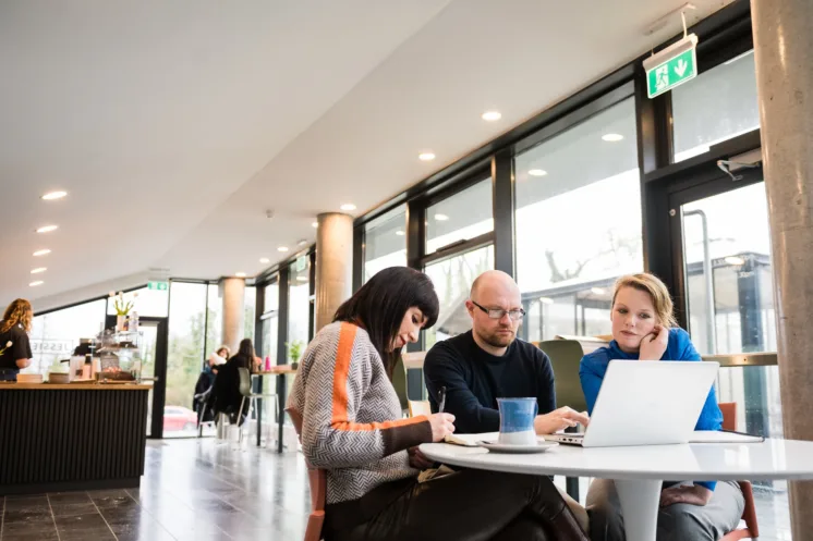 Three mature students working on a group project around a laptop in a café setting