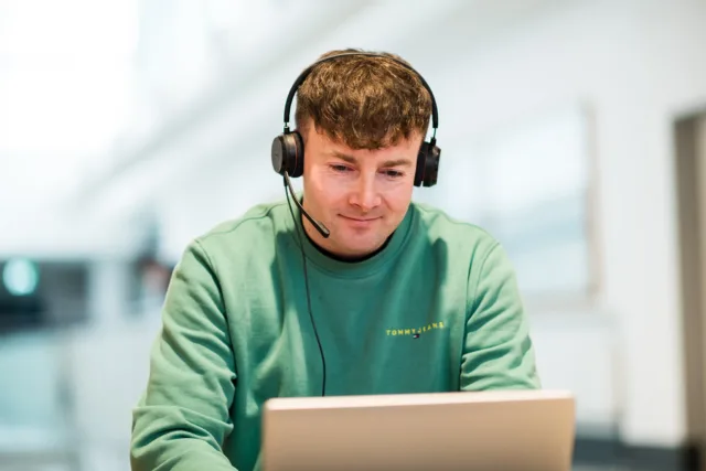 Male student in green jumper and headphones attending online lecture on his laptop
