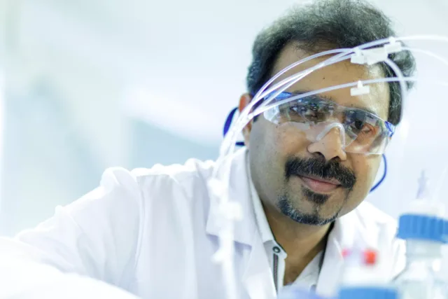 Researcher close up of face with goggles and labcoat.
