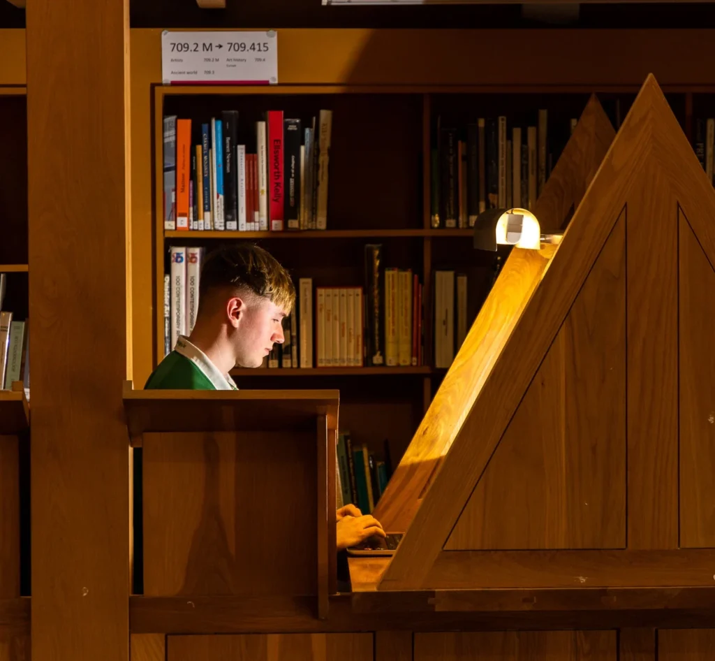 Male student at a desk with desk light in library